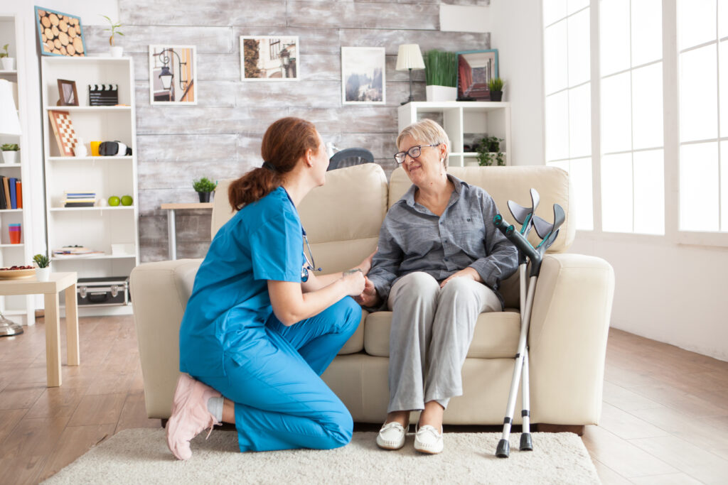 happy old woman nursing home sitting couch talking with her caretaker retired woman with crutches
